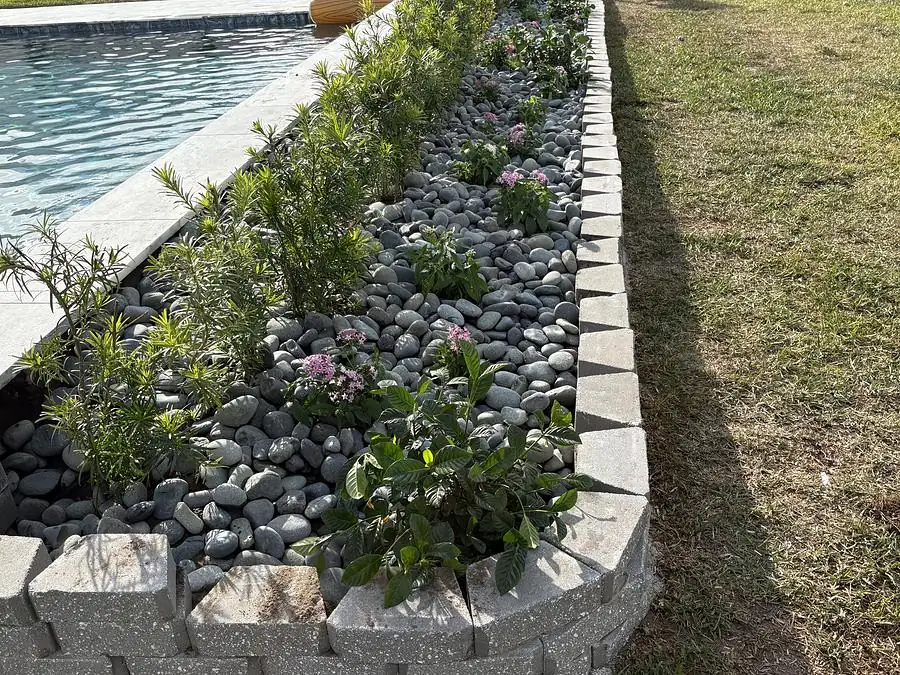Curved block retaining wall planter filled with dark river rock and flowering plants