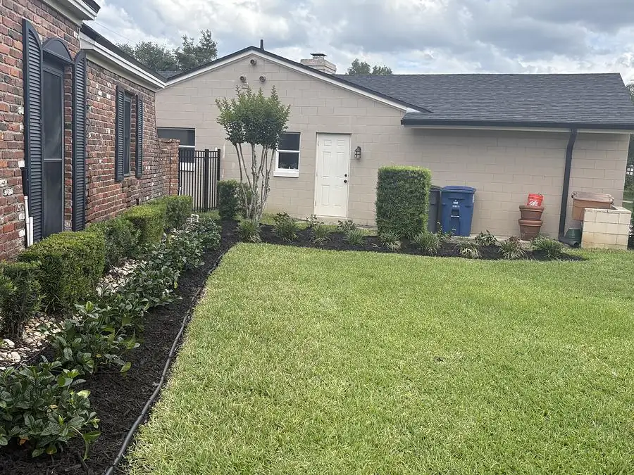 Trimmed hedge row and mulch bed along the front of a brick house with a cut lawn