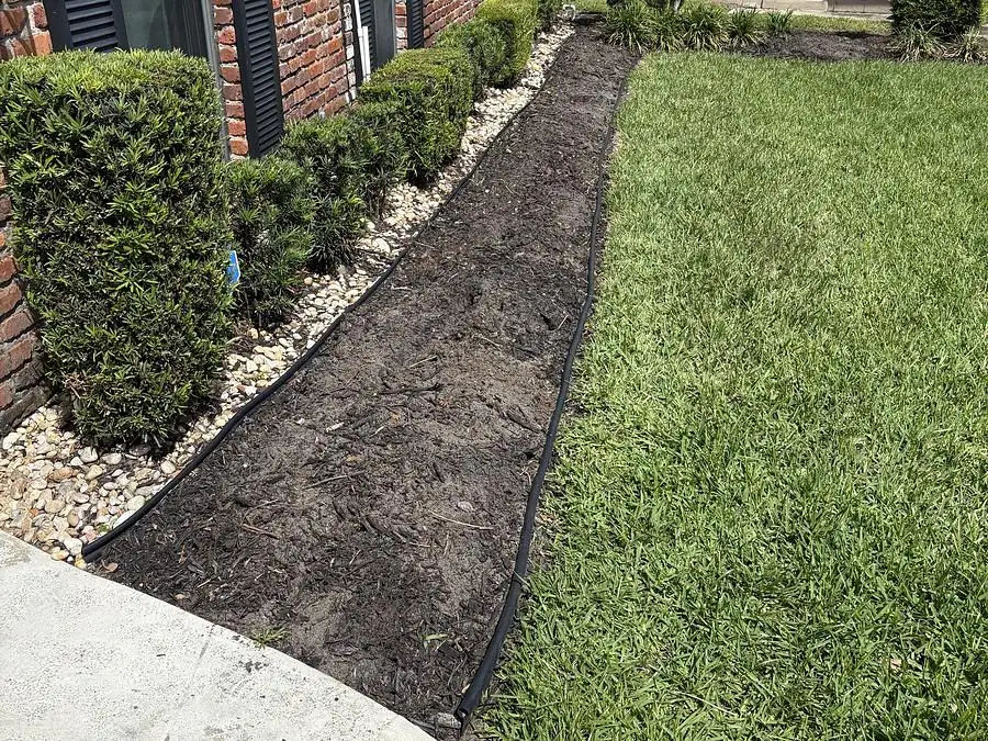 Fresh dark mulch bed and trimmed shrubs beside a walkway at a brick home