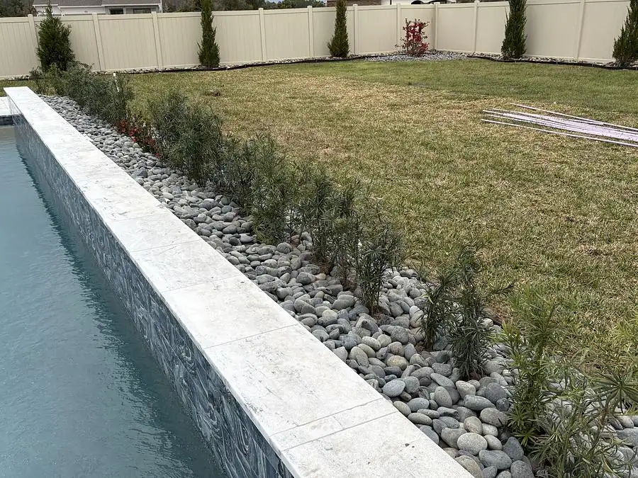 River rock border and new hedge planting running the length of a pool deck