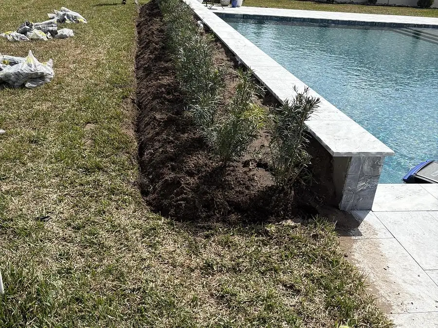 Retaining wall block being installed alongside a pool with a freshly cut planting trench