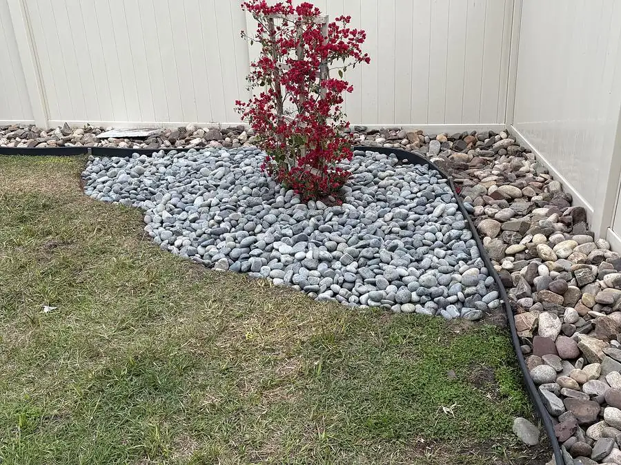 Corner bed of white river rock with a red flowering shrub against a white fence