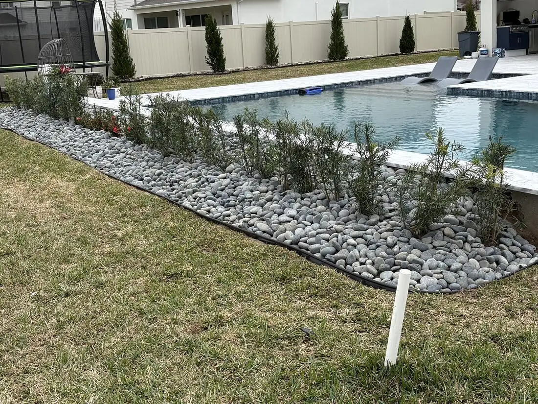 Finished planted bed along the pool filled with river rock and an even hedge row